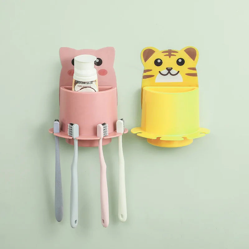 Two wall-mounted toothbrush holders, one pink with a cat design and one yellow with a tiger design, on a light green background.